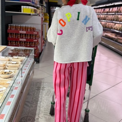 Pessoa com sweat cinza claro e calças riscas rosa e vermelhas a empurrar carrinho em supermercado