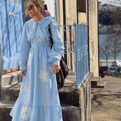 Vestido comprido azul claro com riscas e flores brancas, gola larga e manga comprida.