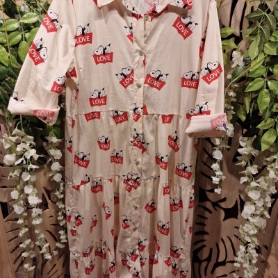 Vestido bege com padrão de panda e placas LOVE vermelho, pendurado numa parede com plantas