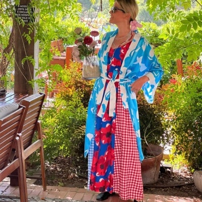 Mulher com vestido longo colorido e kimono azul claro em ambiente exterior com vegetação.