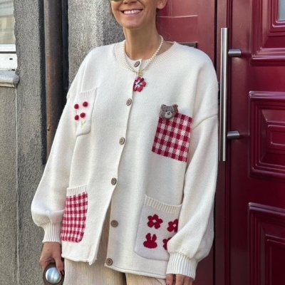 Casaco de malha branco com bolsos vermelhos e detalhes decorativos usados por mulher junto a porta vermelha