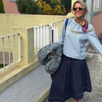 Mulher a usar blusa azul clara, saia azul escura, lenço colorido e sapatos marrons