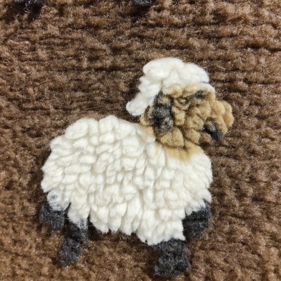 Tapete castanho com padrão texturado de ovelha feita com fios felpudos brancos, castanhos e pretos