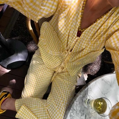 Conjunto de roupa amarelo e branco xadrez com bolso frontal numa mesa ao ar livre com bebida