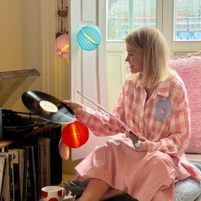 Pessoa com pijama rosa e azul segurando disco de vinil perto de gira-discos com luzes coloridas e caneca