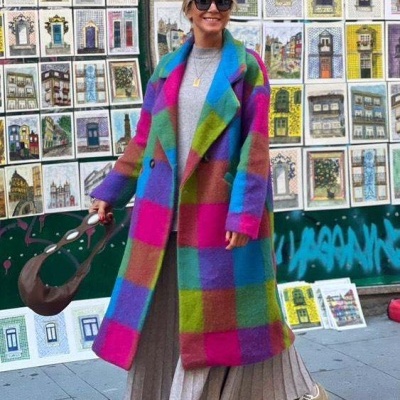 Mulher com casaco xadrez colorido ao pé de várias pinturas