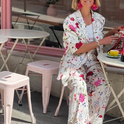 Mulher com conjunto floral branco em esplanada com mesas e bancos rosa claro.