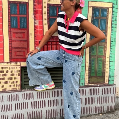 Mulher com camisa às riscas e calças de ganga com corações ao pé de parede colorida