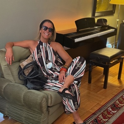 Mulher com vestido colorido sentada em sofá verde, com piano ao fundo.