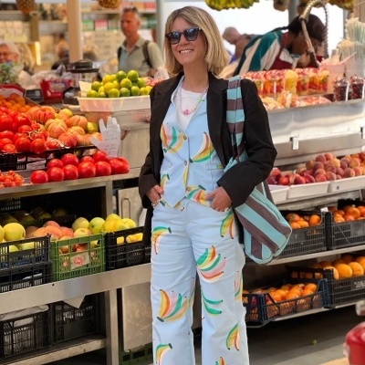 Mulher com roupa colorida e bolsa às riscas numa mercearia com frutas frescas