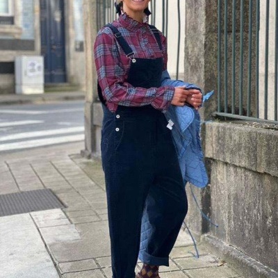 Mulher de blusa xadrez e jardineira preta na rua segurando casaco azul claro