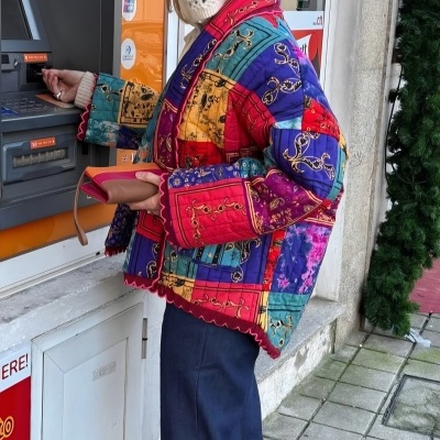 Pessoa com boina branca e casaco colorido usa caixa multibanco na rua