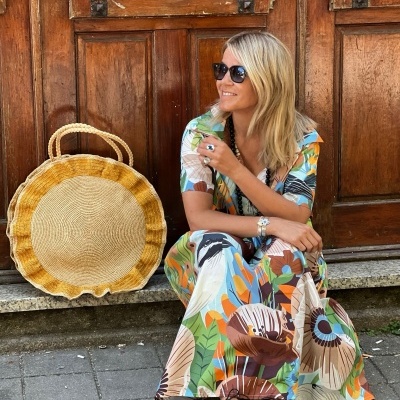 Mulher sentada com vestido floral colorido e bolsa redonda de materiais trançados ao lado