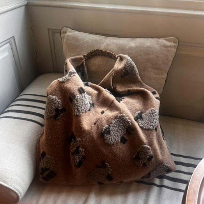 Mala de tecido castanho com padrão de ovelhas sentada numa cadeira estofada creme