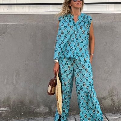 mulher com conjunto azul floral e acessórios castanhos em ambiente urbano