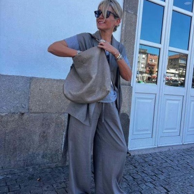 Mulher com conjunto de roupa cinzenta e mala grande cinzenta em ambiente urbano