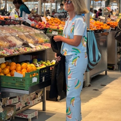 Mulher com fato estampado de bananas num mercado de fruta com várias frutas expostas