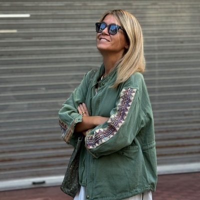 Casaco verde com padrão vestido branco e óculos escuros em fundo portão metálico