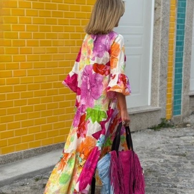 Pessoa de costas com roupa comprida floral colorida e mala rosa com franjas