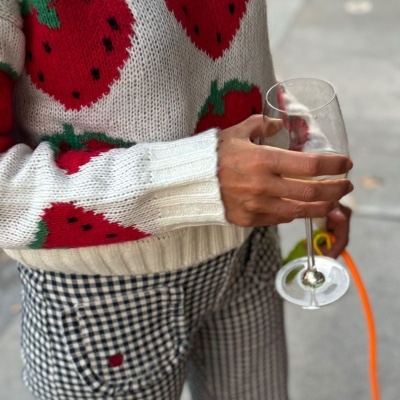 Camisola branca de malha com morangos vermelhos, calças xadrez e taça de vidro na mão