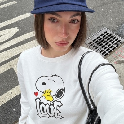 Pessoa com sweatshirt branca com desenho do Snoopy e palavra LOVE e boné azul com texto branco