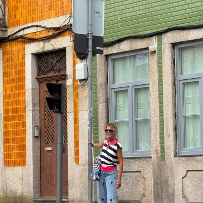 Sinal de trânsito cinzento com texto 'CMP' em rua com paredes azulejadas laranja e verde e mulher vestida casual