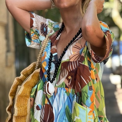 Vestido colorido tropical com bolsa amarela e colar preto.