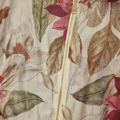 Casaco leve com padrão floral em tons castanhos, verdes e vermelhos sobre fundo bege com fecho dourado e capuz.