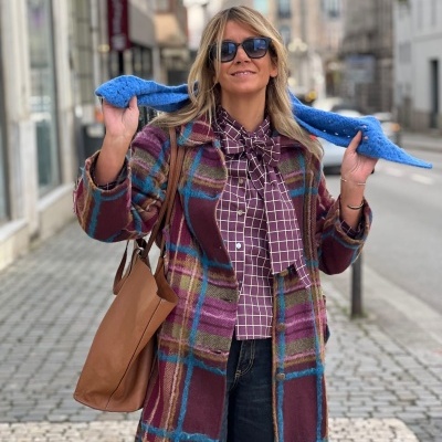 Mulher com casaco xadrez bordeaux, camisa com laço e óculos de sol