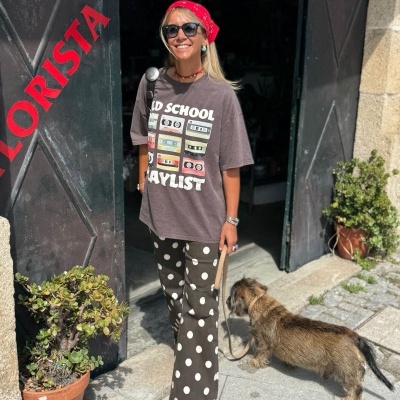 Mulher com roupa casual e cão junto a porta de loja preta com texto vermelho FLORISTA