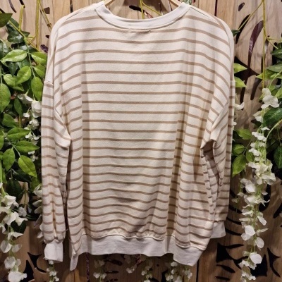 Camisola creme com riscas horizontais castanhas pendurada em cabide de madeira com fundo decorativo