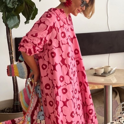 Vestido rosa com flores grandes e bolsa de croché colorida em ambiente interior.