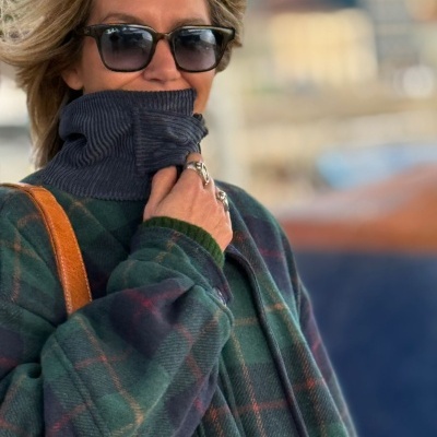 Pessoa com casaco às riscas e gola alta azul, óculos escuros e anéis prateados