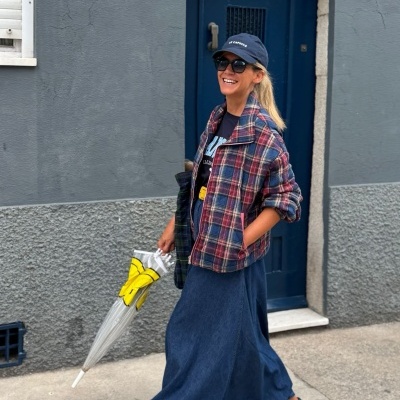 Mulher com casaco xadrez e saia azul junto a porta azul escura