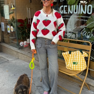Mulher com camisola de malha de morangos e calças xadrez com cão e saco amarelo próximo.