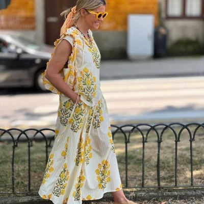 Mulher a usar vestido florido amarelo e branco com sapatos bege e óculos de sol amarelos