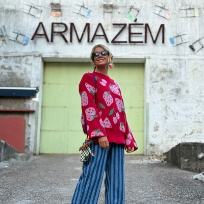 Mulher com camisola vermelha de morangos em frente a armazém com parede branca e porta verde