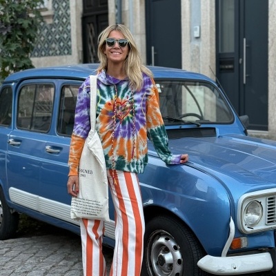 Pessoa com roupa colorida ao lado de carro azul antigo na calçada