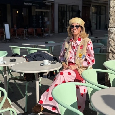 Mulher com vestido rosa de bolinhas vermelhas num café ao ar livre com mesas e cadeiras verde-menta