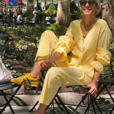 Mulher com conjunto amarelo xadrez e ténis amarelos sentada em cadeira preta no parque