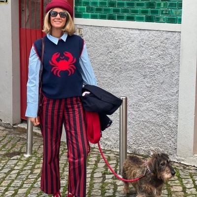 Mulher em roupa colorida com cão pequeno de trela vermelha numa rua de calçada