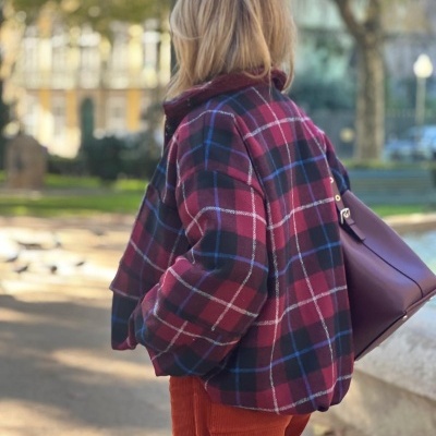 Mulher de costas com casaco xadrez vinho e mala roxa num parque