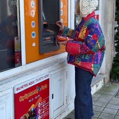 Pessoa a usar caixa multibanco com casaco colorido e capuz de croché