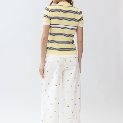 Mulher de costas com camisola polo de riscas amarelas, brancas e pretas e calças largas brancas com padrão de limões amarelos