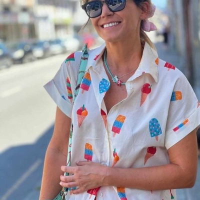 Camisa feminina branca curta com estampado de sorvetes coloridos usada por mulher com óculos de sol na rua