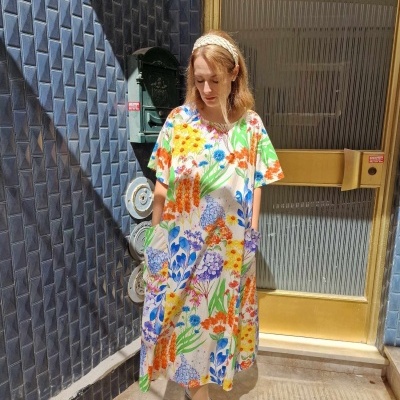 Vestido solto floral colorido em fundo branco usado por mulher em porta de vidro dourada e parede azul