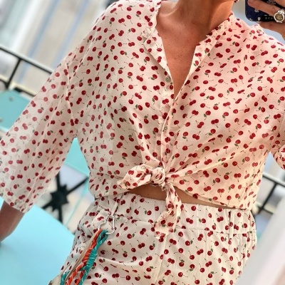 Conjunto branco com padrão de cerejas vermelhas, blusa com nó e saia com cinto colorido