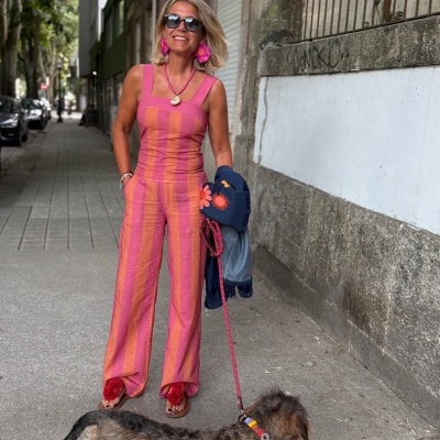 Mulher com macacão listrado rosa e laranja e sandálias com pompons vermelhos a passear com cão