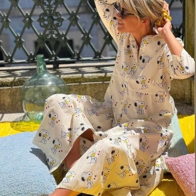 Criança de vestido comprido bege com estampado de cães sentada em almofadas coloridas ao ar livre.