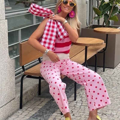 Mulher sentada com roupa colorida e padrão de bolinhas e riscas numa esplanada urbana